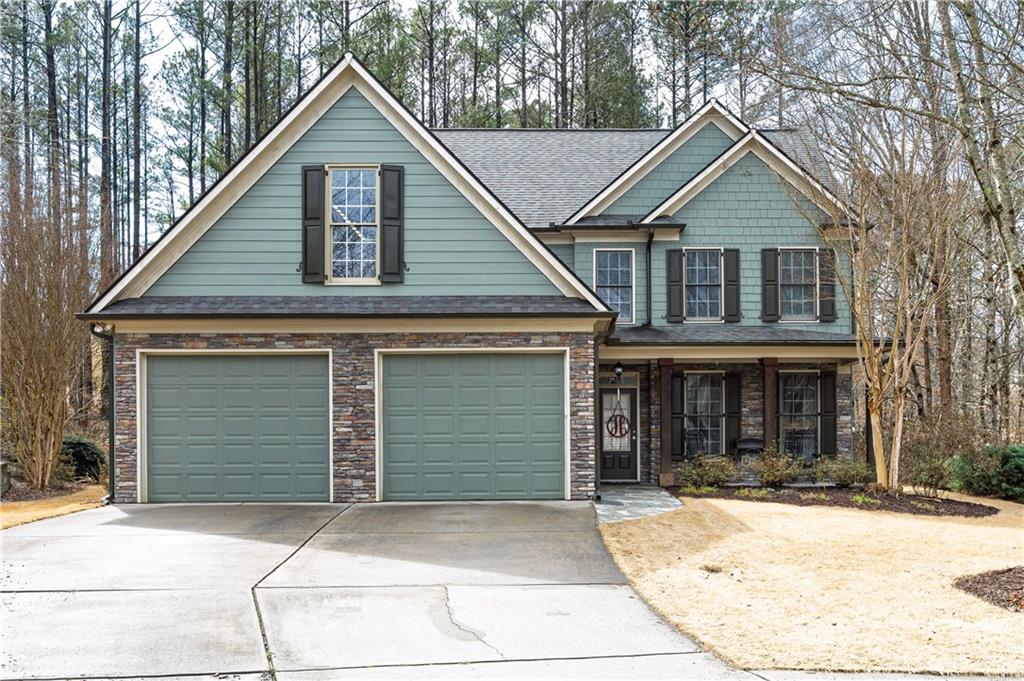 Sage-green two-story home with stone accents and a two-car garage among leafless trees.