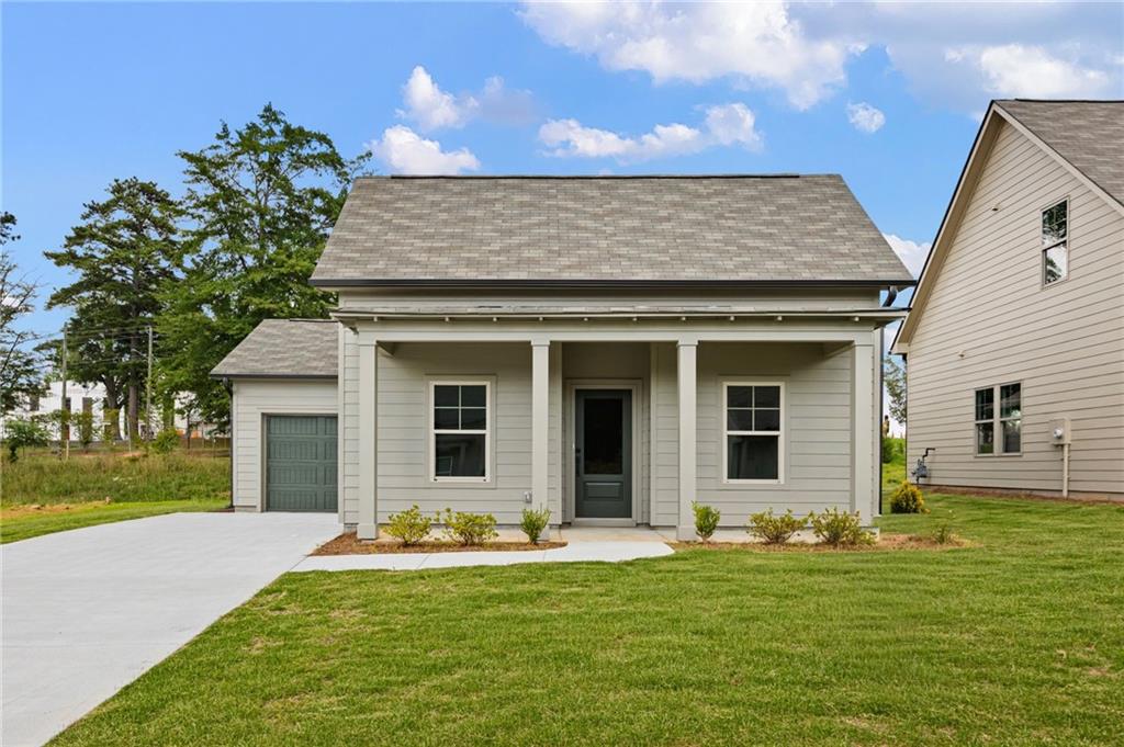 Light-colored house with a covered porch, attached garage, and broad concrete driveway.