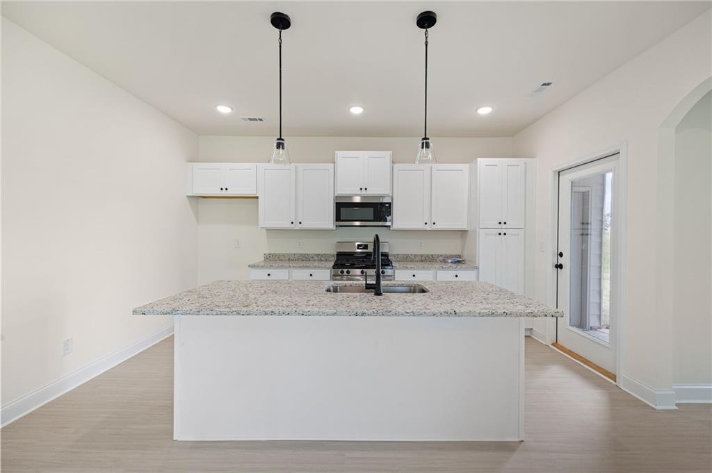 Vacant kitchen with a large granite island, white cabinetry, and stainless steel appliances.