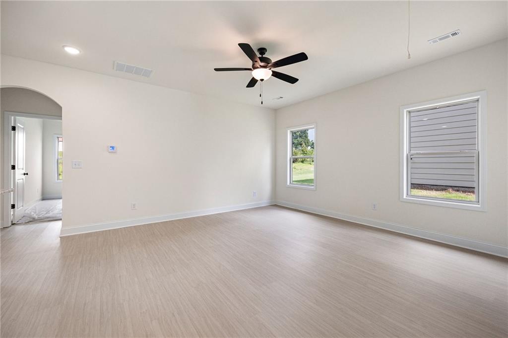 Vacant interior room with pale flooring, a black ceiling fan, and two windows.