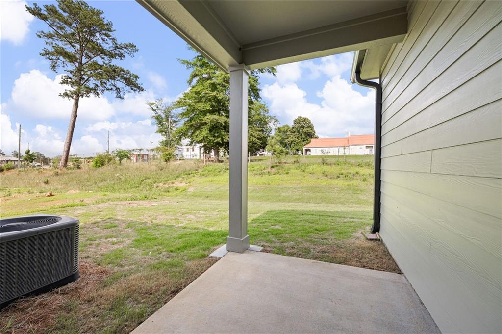 Covered concrete patio overlooking a grassy yard with mature trees.