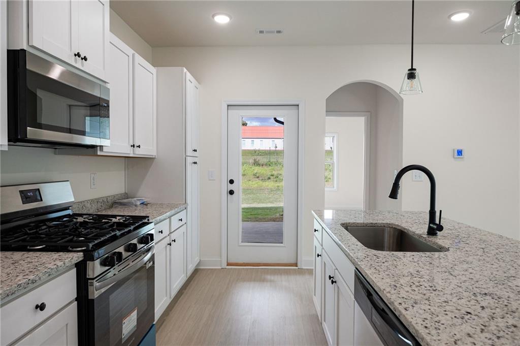 Kitchen with white cabinets, stone counters, a sink island, and stainless steel appliances.