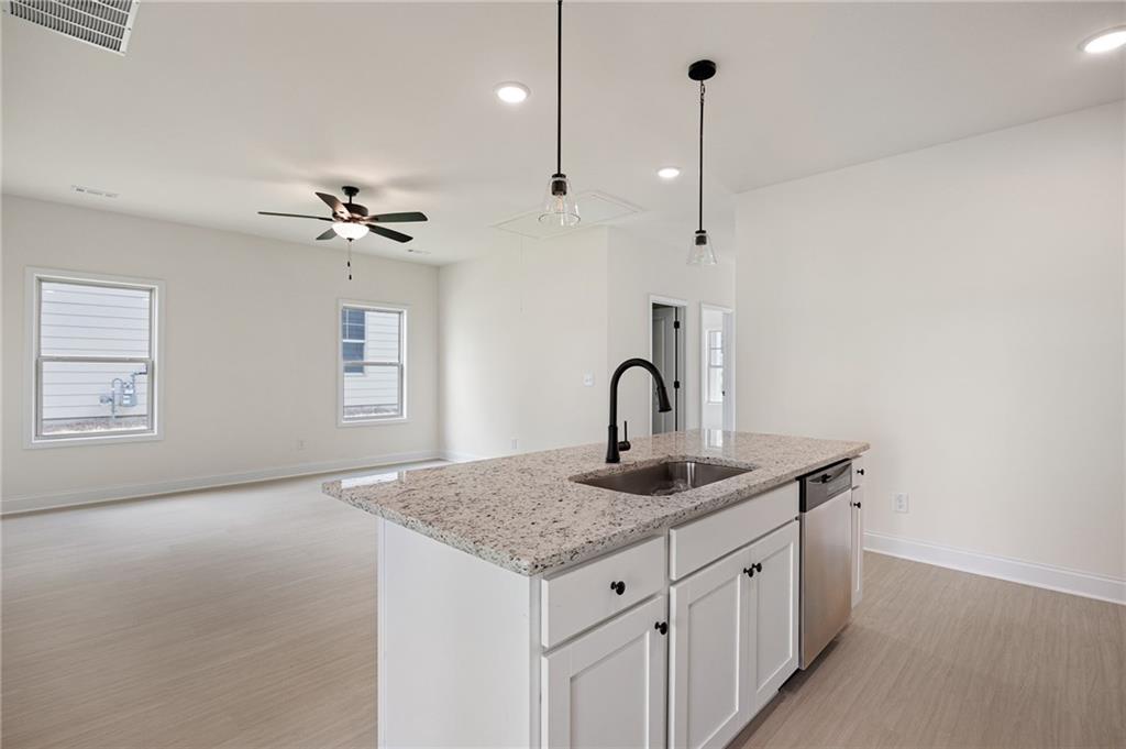Vacant kitchen with a granite island, black faucet, and stainless-steel dishwasher opening to a living area.
