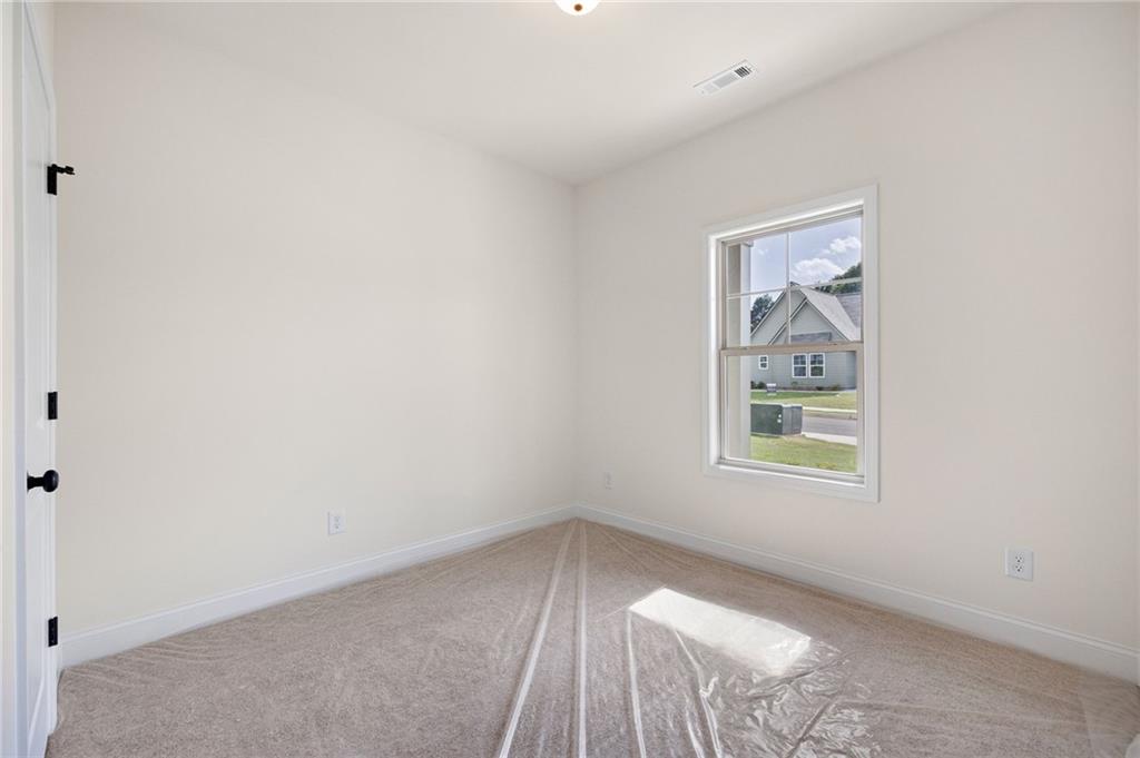 Empty bedroom with beige carpet and a window overlooking neighboring homes.