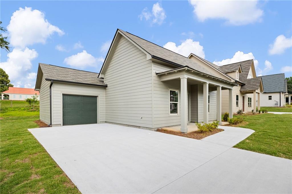 Home with a covered front porch, dark green garage door, and broad concrete driveway.