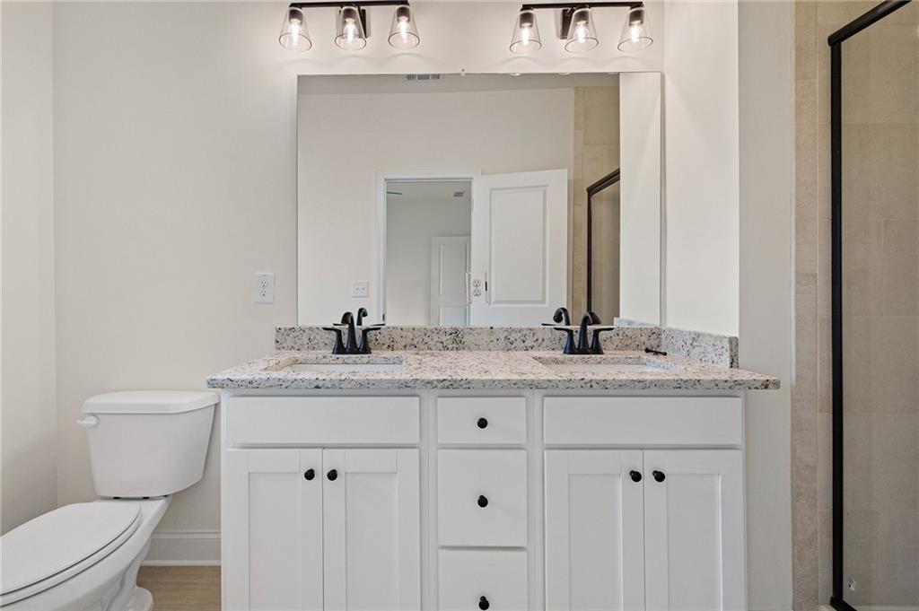 Bathroom with a white double vanity, speckled granite countertop, and glass-enclosed shower.
