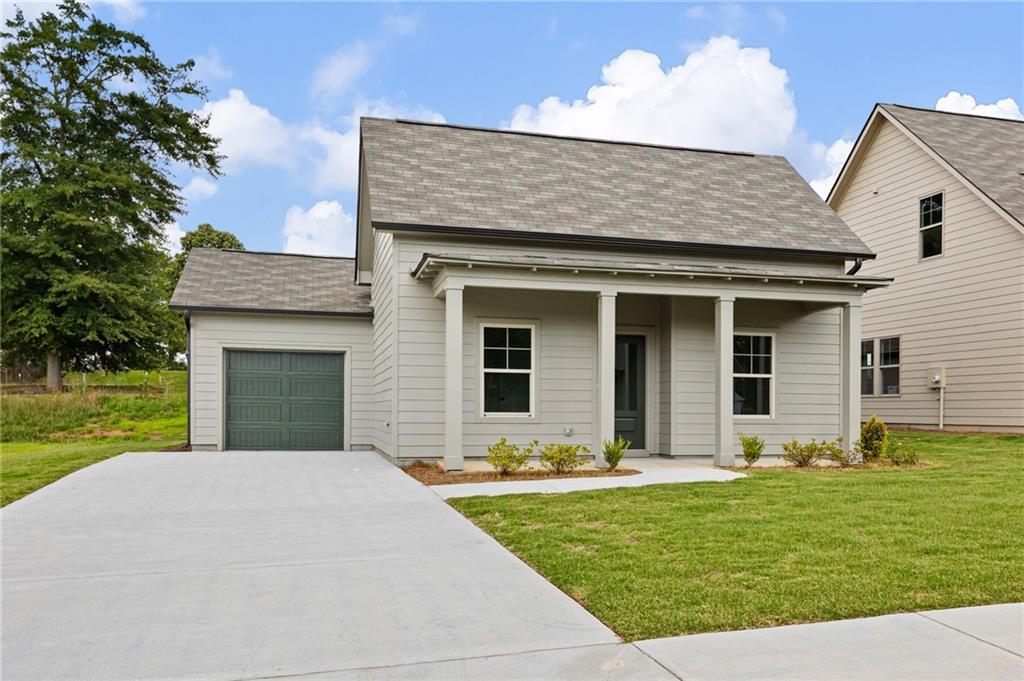 Light-sided house with a covered front porch, attached garage, and broad concrete driveway.