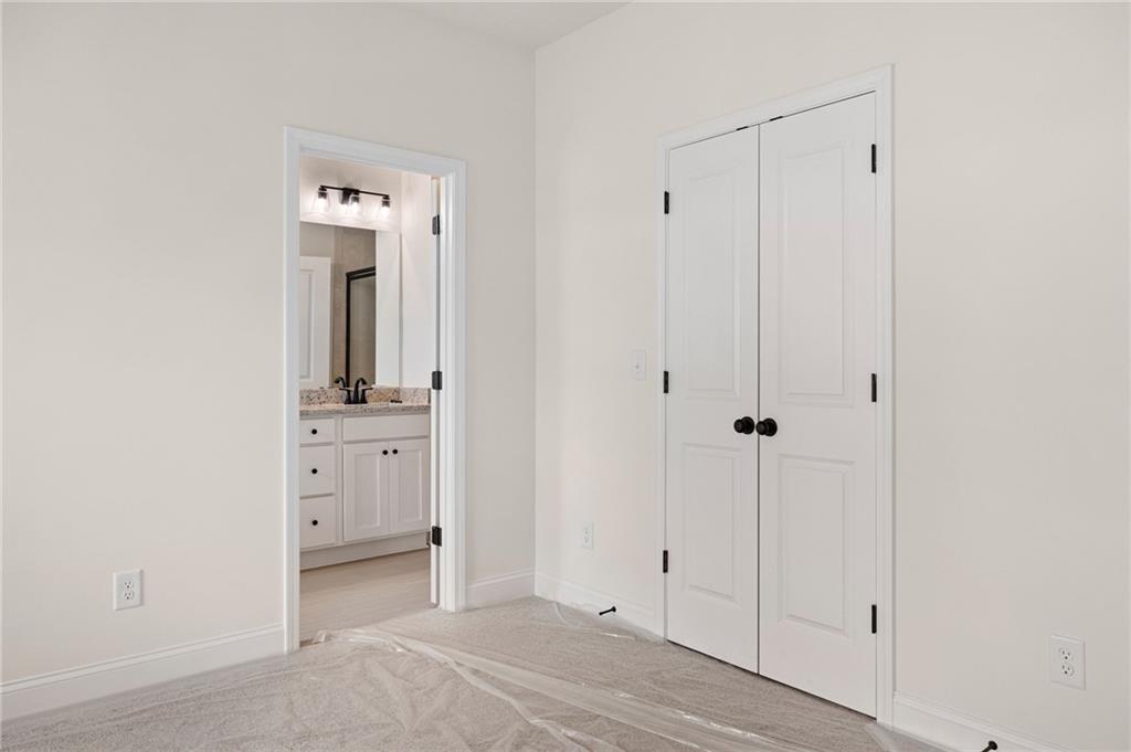 Empty bedroom with white double closet doors and a bathroom vanity visible through the open doorway