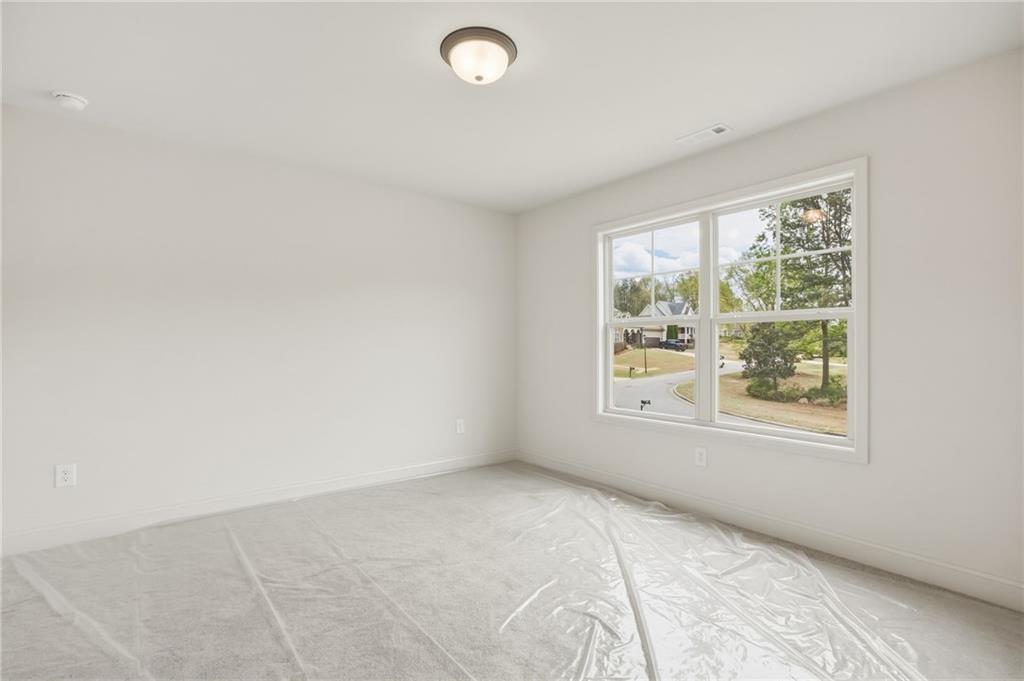Empty bedroom with plastic-covered carpet and a large window overlooking trees and a residential street.