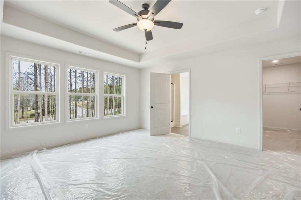 Empty bedroom with a tray ceiling, ceiling fan, three windows, and plastic-covered floor.