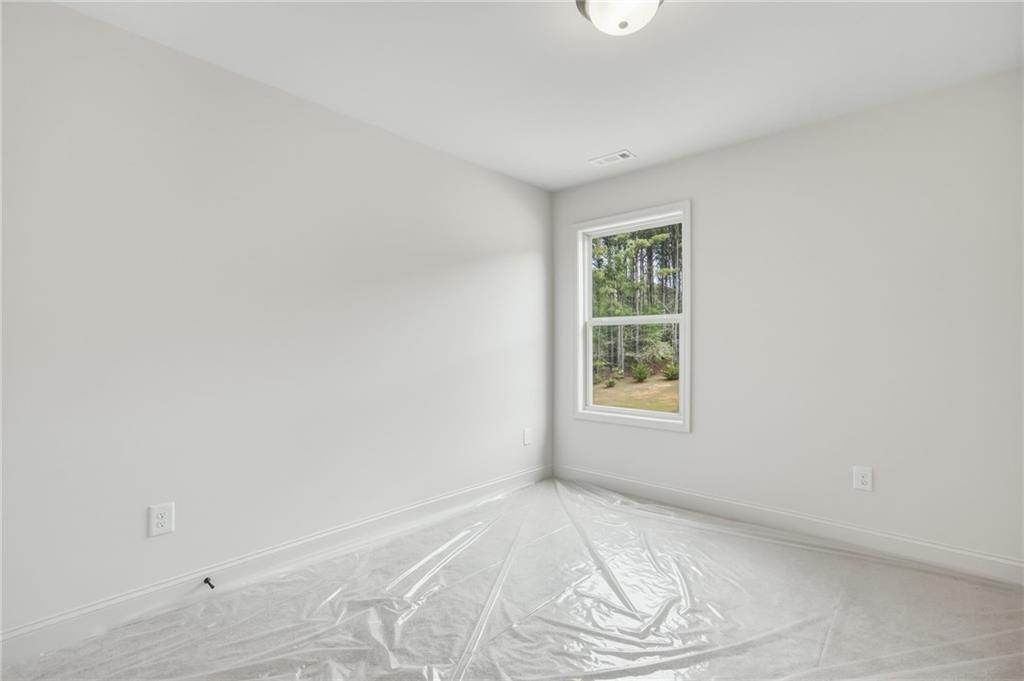 Empty room with white walls, a window overlooking trees, and plastic sheeting across the floor.