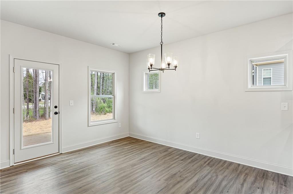 Empty dining area with a chandelier, gray wood-look flooring, and a glass-paneled exterior door.