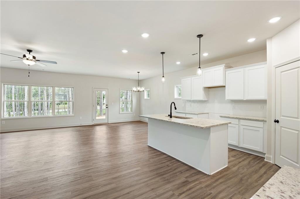 Open kitchen with a large island, white cabinets, wood-look floors, and windows overlooking trees.