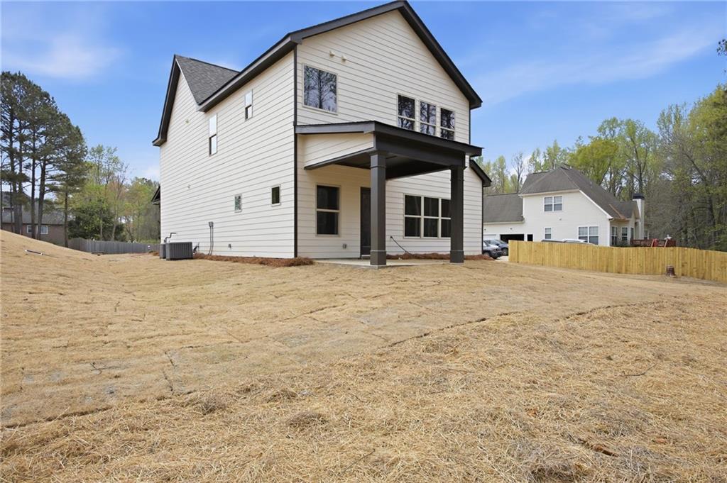 Rear exterior of a two-story white home with a covered patio and broad straw-covered lawn.
