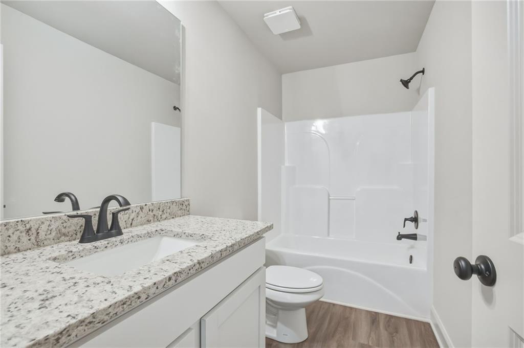 Bathroom with a granite-topped vanity, white tub-shower, dark fixtures, and wood-look flooring.