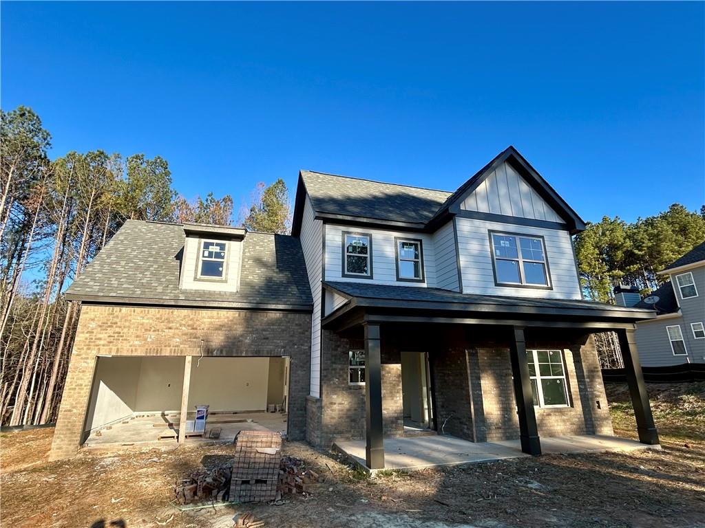 Two-story gray-and-brick house under construction with an open garage and covered porch.