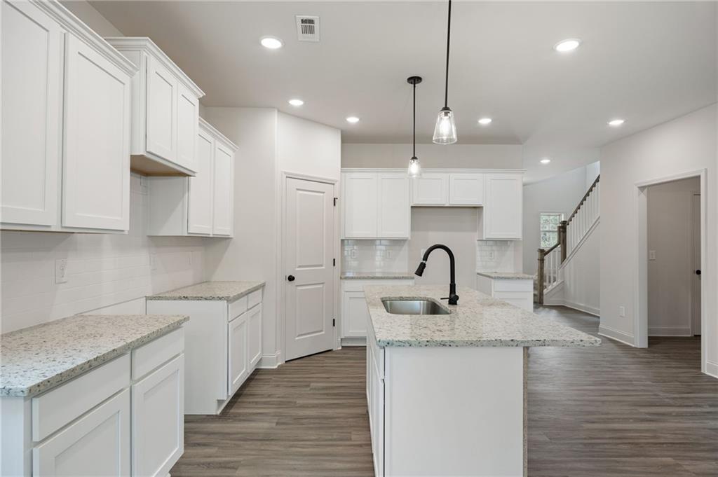 Unfurnished kitchen with white shaker cabinets, stone counters, a large sink island, and dark wood-look floors.