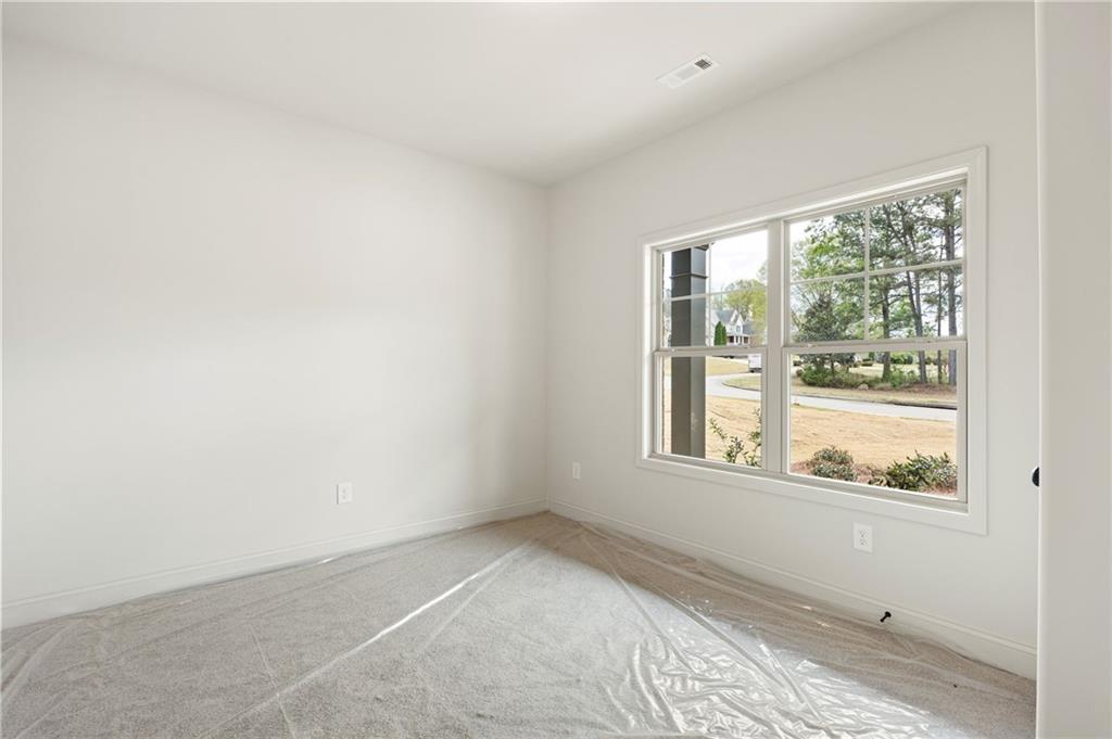 Empty carpeted bedroom with a large window overlooking trees and a street.