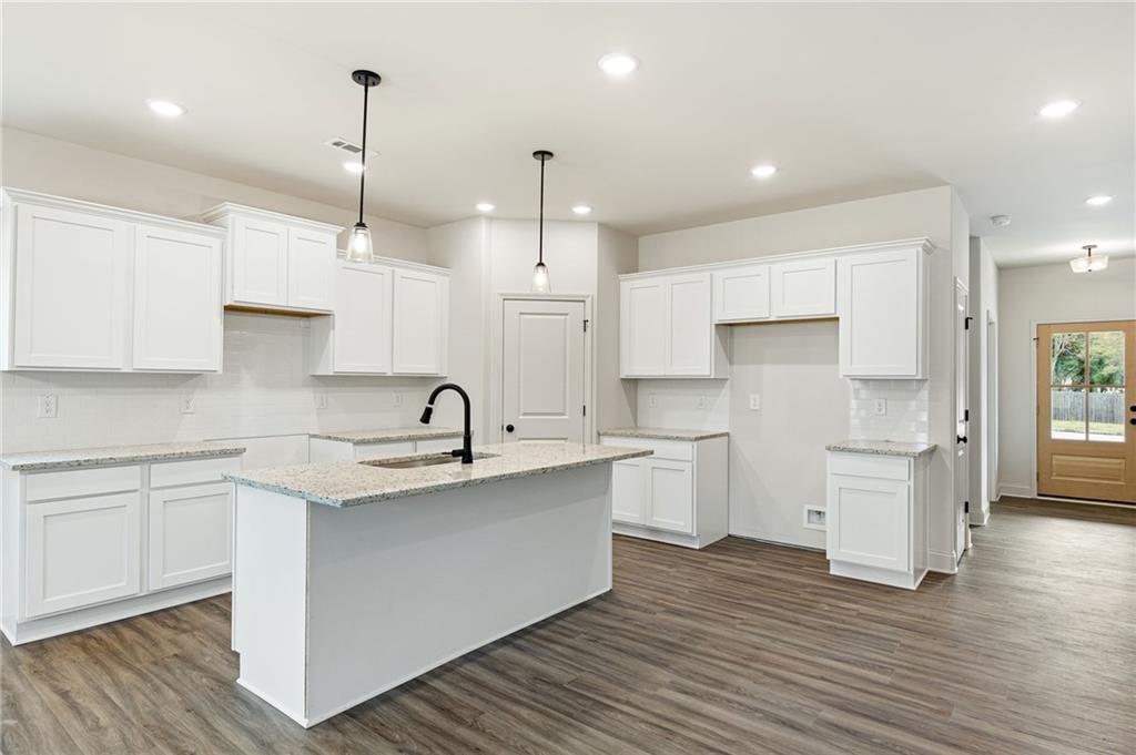 Vacant kitchen with white cabinets, a large stone island, pendant lights, and dark wood-look flooring.