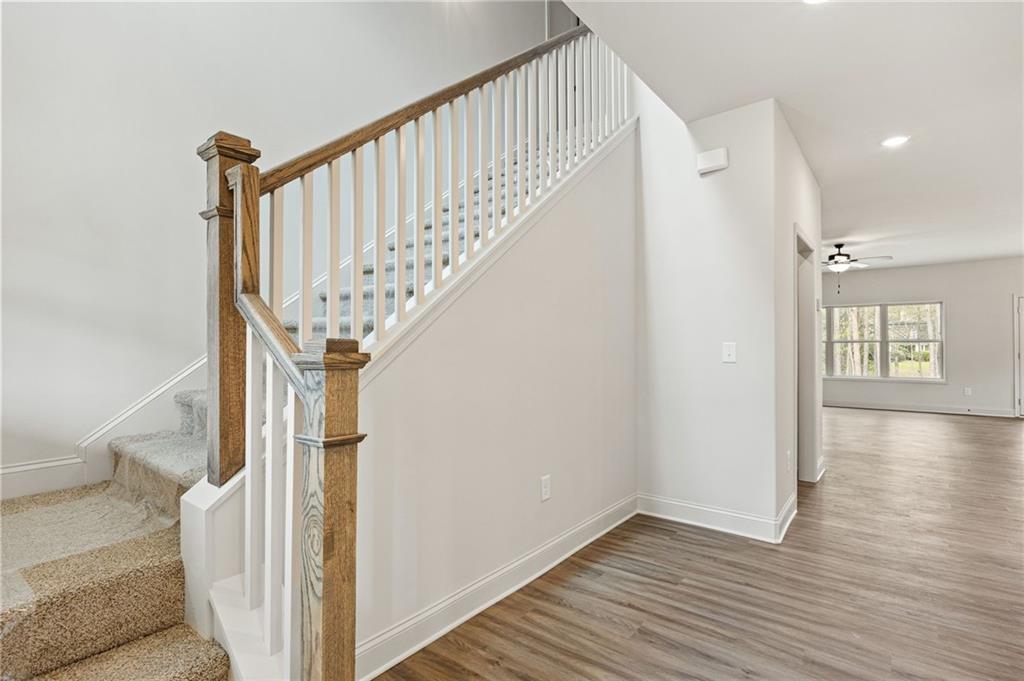Foyer staircase with wood-and-white railing beside an open living area with plank flooring.