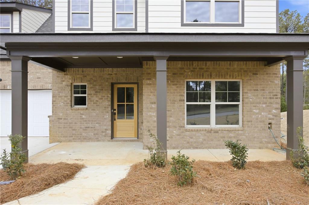 Two-story house with a covered brick porch, wood-and-glass entry door, and pine-straw landscaping.