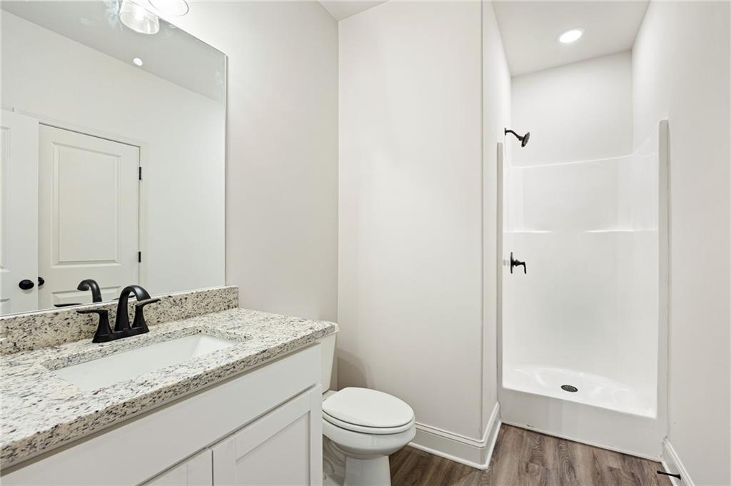 Bathroom with a granite-topped white vanity, toilet, and shower enclosure.