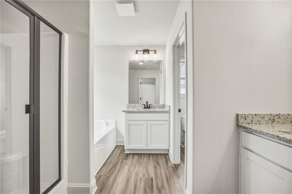 Bathroom with a white vanity, speckled stone countertop, bathtub, and black-framed glass shower.