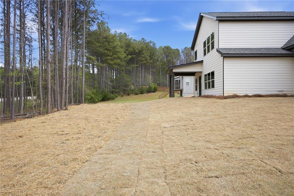 White two-story house beside a straw-covered lawn and wooded tree line.
