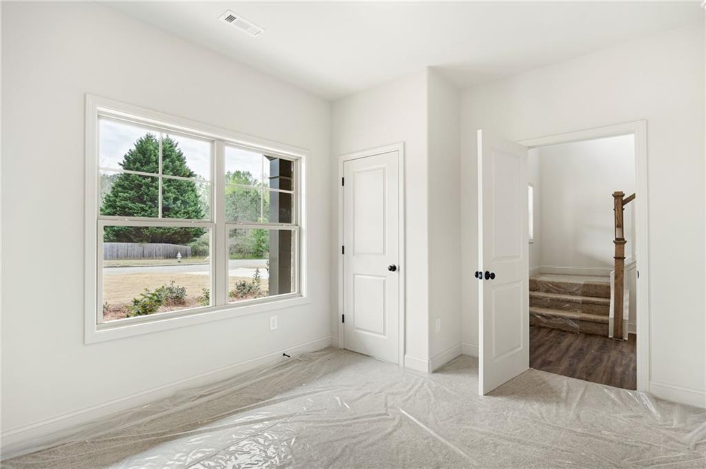 Empty carpeted room with plastic floor covering, a large window, and an open doorway to stairs.