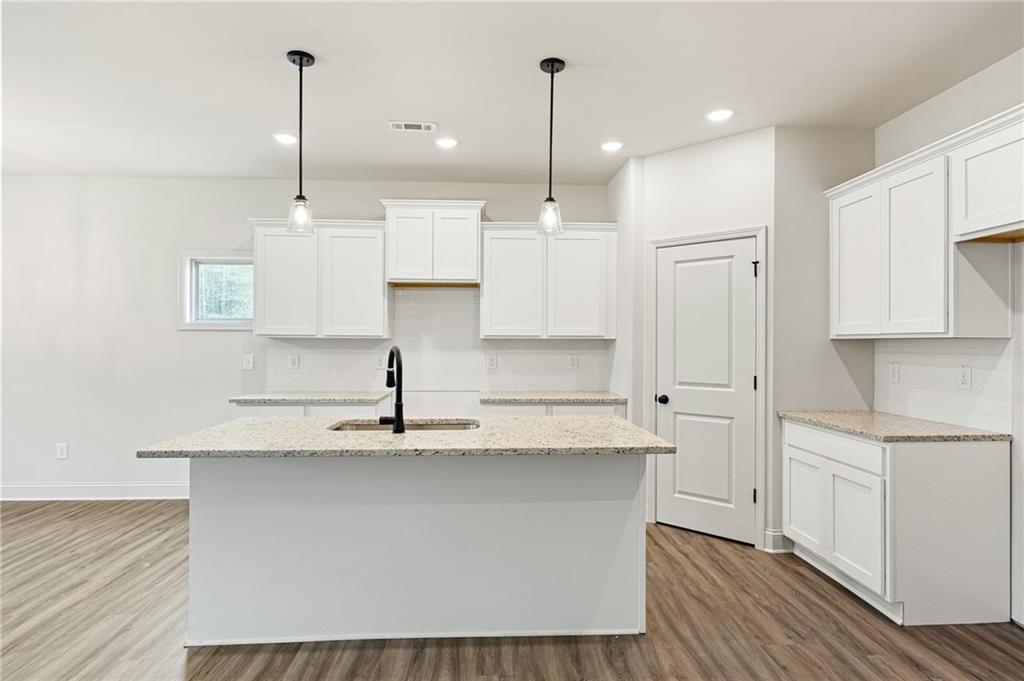 Bright kitchen with a large granite island, white cabinets, pendant lights, and wood-look flooring.
