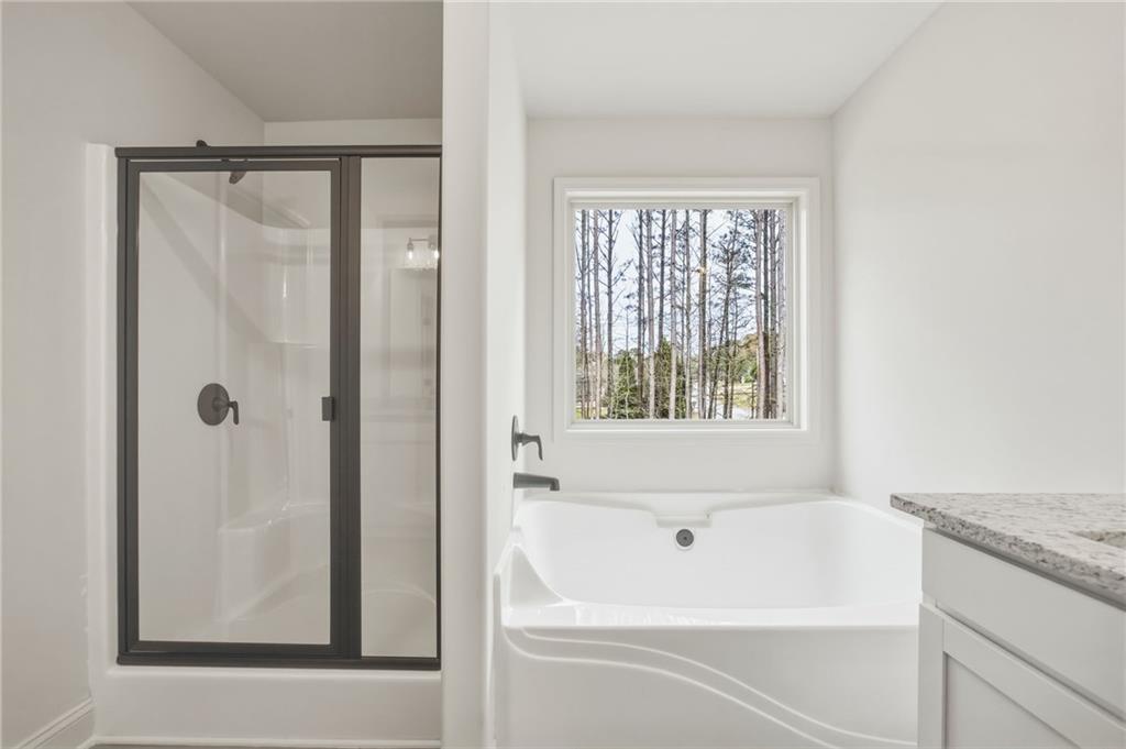 Bathroom with a corner soaking tub beneath a window and a dark-trimmed glass shower.
