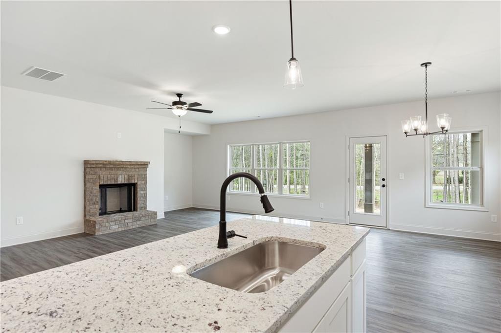Open-plan kitchen and living area with a stone island, brick fireplace, and windows overlooking trees.