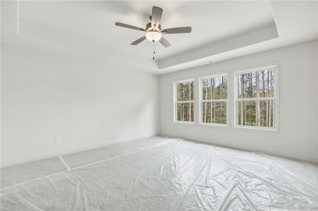 Empty bedroom with a tray ceiling, ceiling fan, three wooded-view windows, and plastic floor covering.