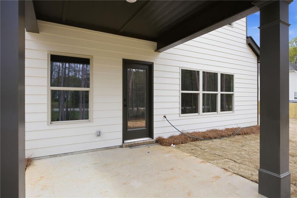 Covered concrete patio with a black-framed glass door and windows on a white-sided house.