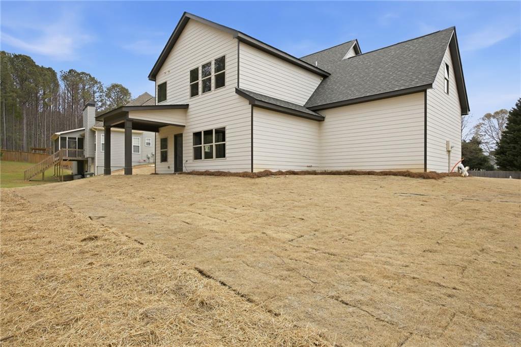 Rear of a white two-story house with dark gabled roofs, a covered patio, and a broad dormant lawn.