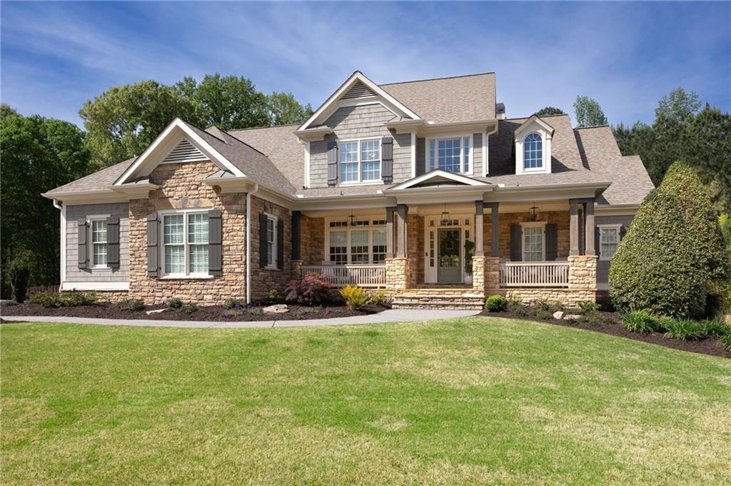 Two-story stone-and-gray home with multiple gables and a covered porch, set behind a broad lawn.