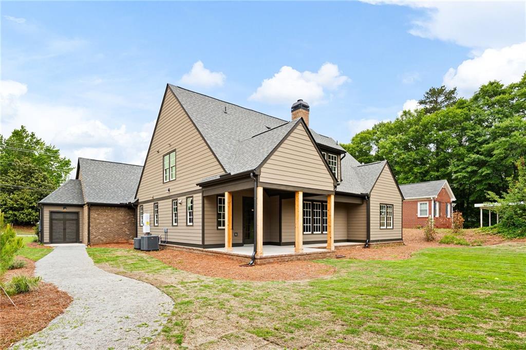 Tan-sided house with a covered porch, attached garage, and curved gravel walkway across the lawn.