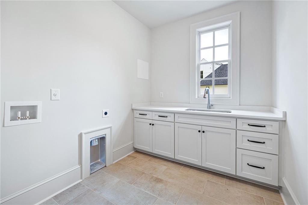 Laundry room with white cabinets, a sink beneath a window, washer hookups, and a small pet door.