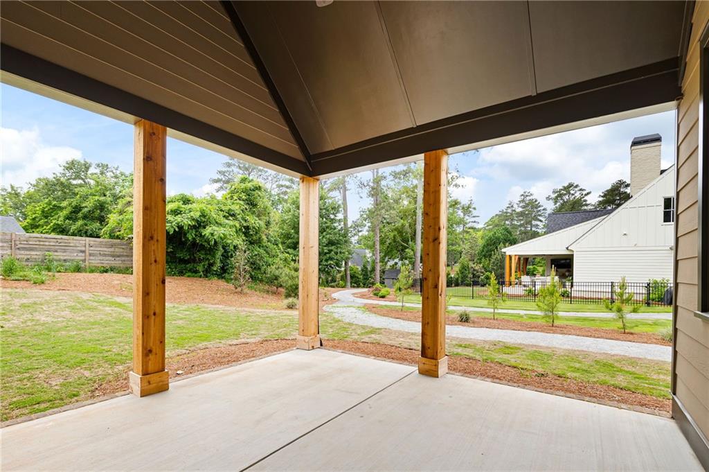 Covered concrete patio with wooden posts overlooking a grassy yard and gravel path.