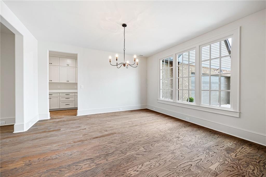 Empty dining room with hardwood floors, a chandelier, and large windows beside the kitchen.