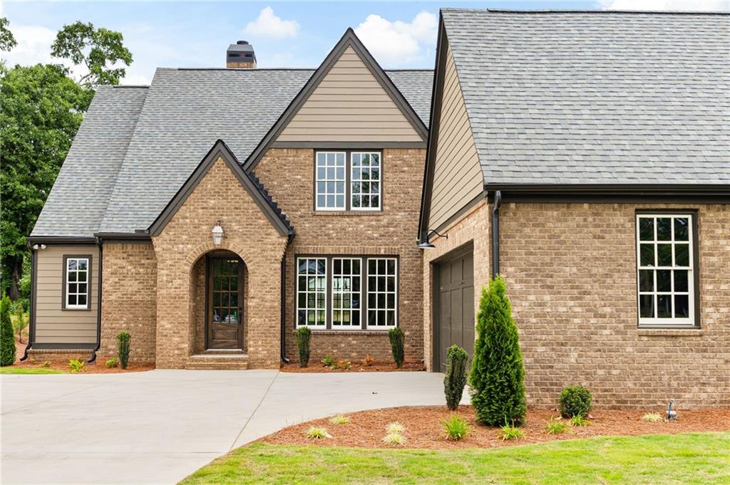Brick house with steep gray gables, an arched entrance, and a broad concrete driveway.