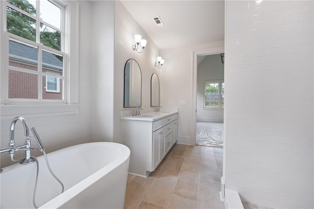 Bathroom with a freestanding soaking tub, double-sink vanity, and tall arched mirrors.