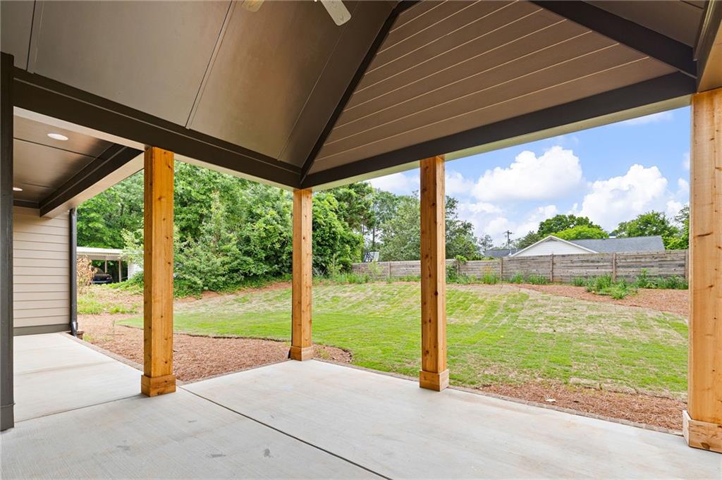 Covered concrete patio with wooden posts overlooking a fenced backyard.