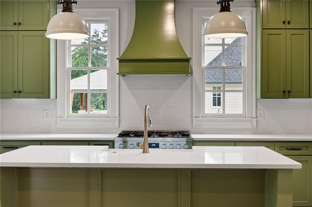 Kitchen with sage-green cabinets, a white island, gas range, and two windows.