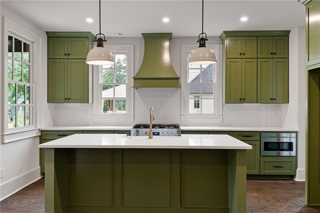 Kitchen with olive-green cabinets, a white island, stainless-steel appliances, and a matching range hood.