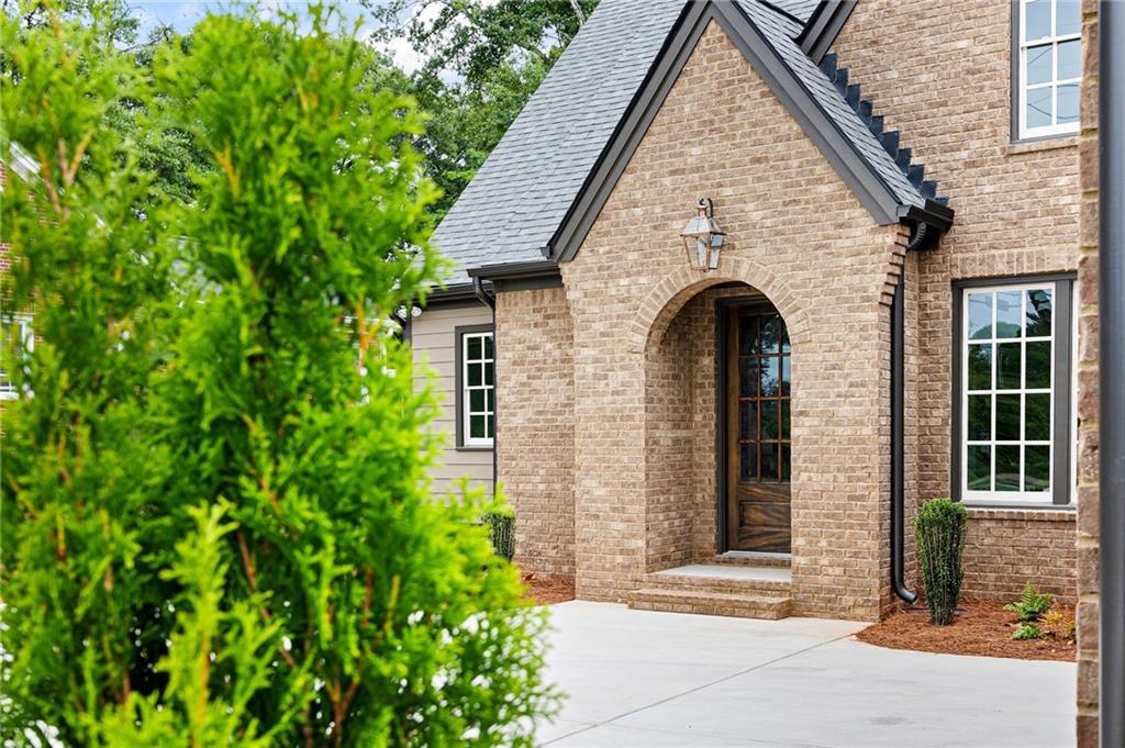 Brick home entrance with an arched doorway, dark wood door, and landscaped front walk.