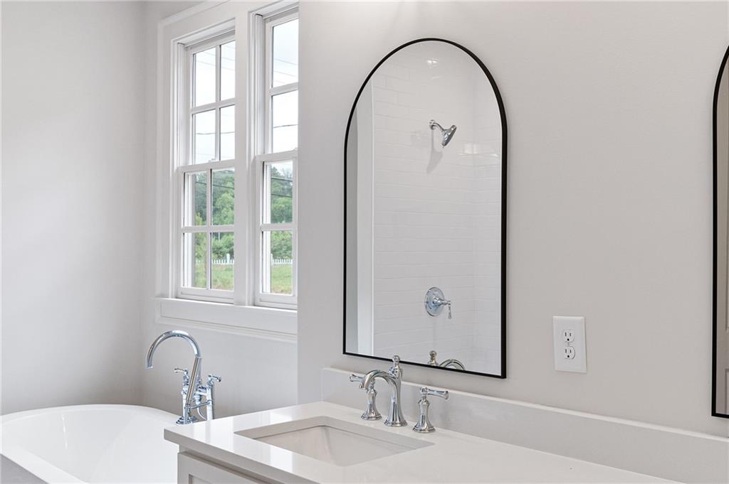Bright bathroom with an arched black-framed mirror, white vanity, soaking tub, and tall windows.