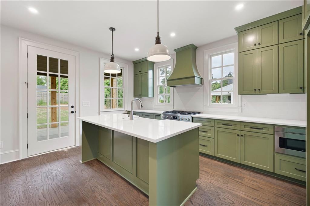 Kitchen with sage-green cabinets, a large white island, stainless steel range, and hardwood floors.