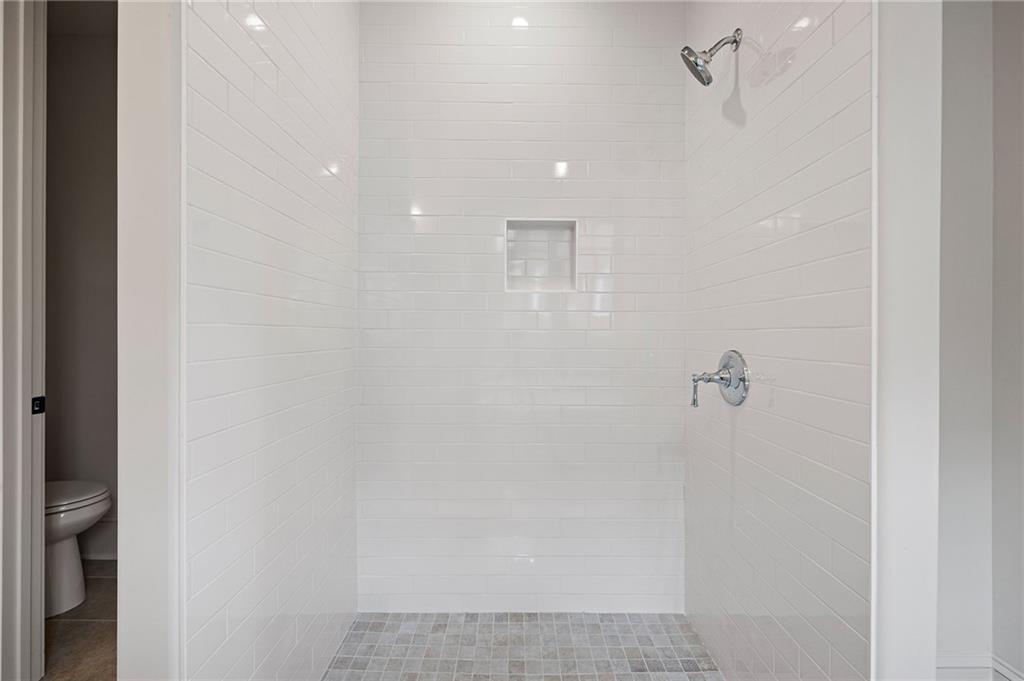 Walk-in shower with white tile walls, a recessed niche, and a gray mosaic floor.