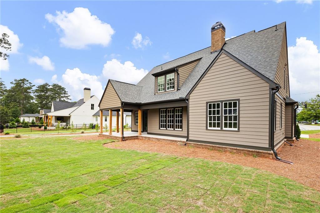 Two-story taupe-sided home with a covered porch, brick chimney, and broad lawn.